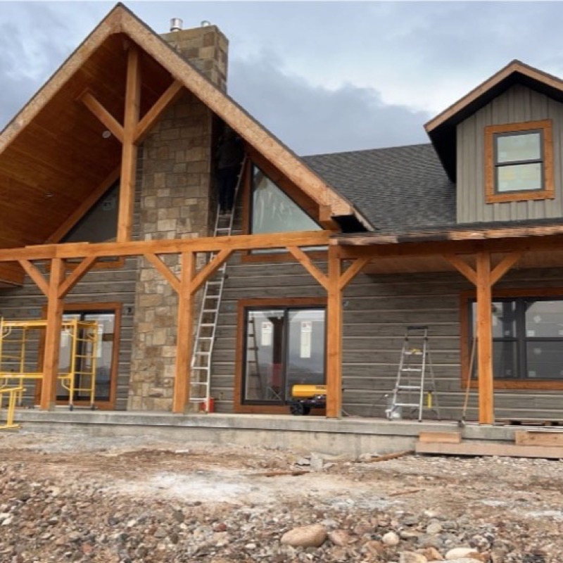 Custom home exterior with stone, timber trim, and siding under finish work