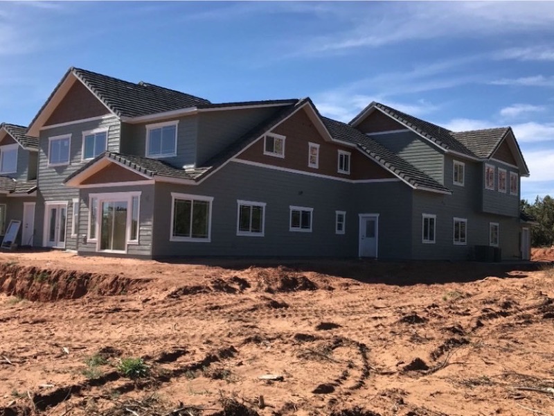 Multi-story home with grey siding, white trim, and red rock accents in a desert setting
